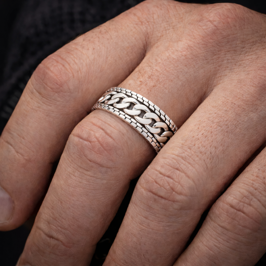 A close-up of a person's hand wearing a silver ring with a chain-like design.