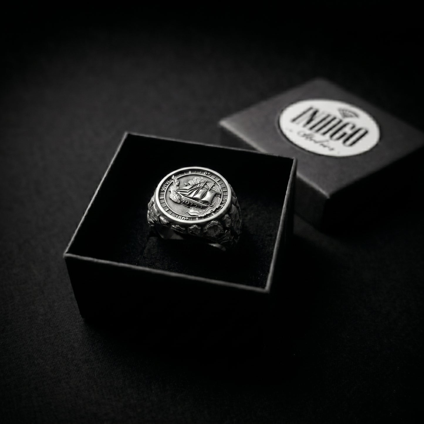 Antarctica explorer signet ring in solid sterling silver 925 featuring a detailed sailing ship over a map of Antarctica, surrounded by directional markings. The ring has a deep oxidized finish with strong contrast, highlighting fine handcrafted textures and relief details. Shot on a dark stone background to emphasize its bold, masculine design, adventure theme, and expedition spirit. Unique nautical jewelry piece inspired by travel, ocean journeys, and exploration beyond the known world.