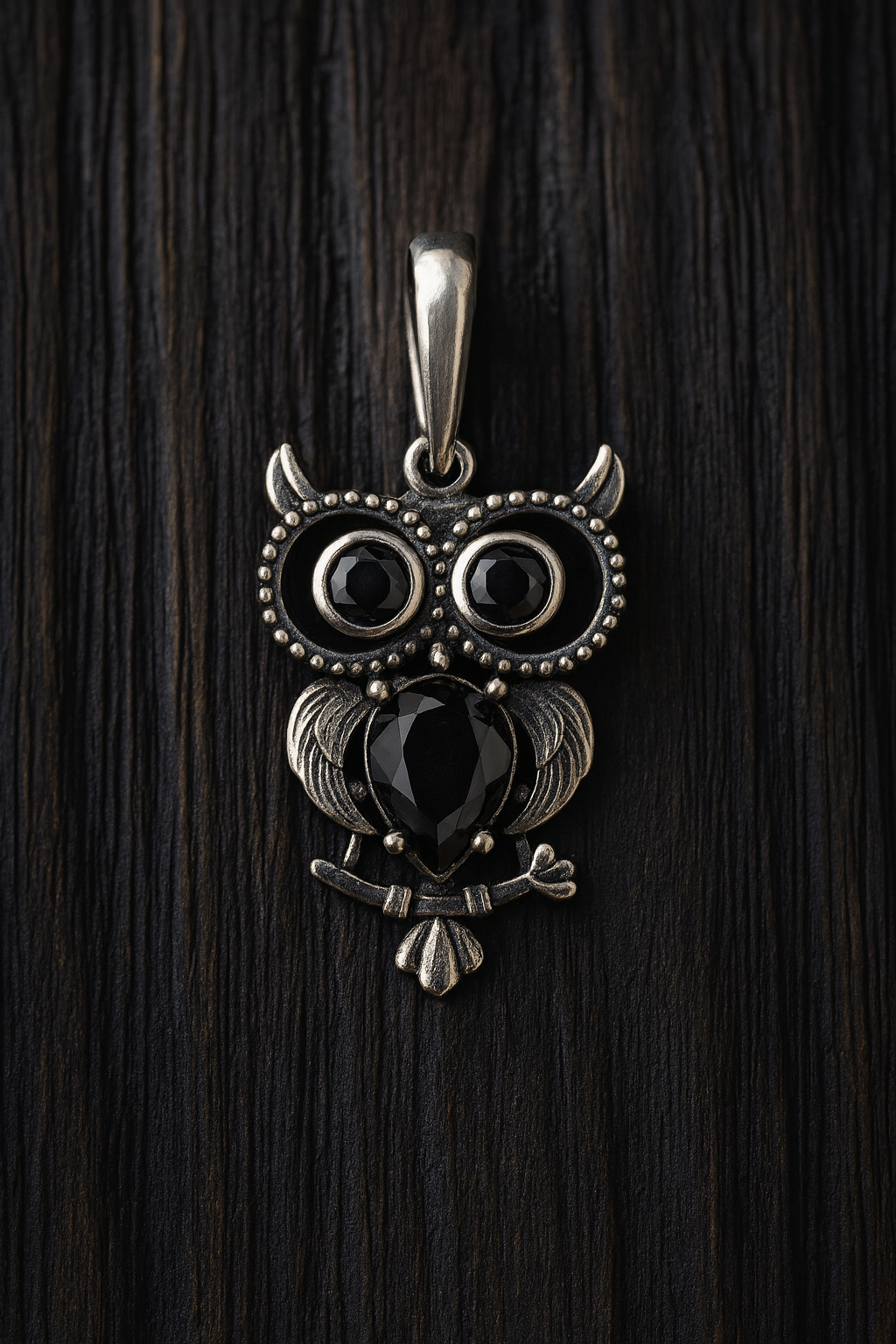 A silver pendant in the shape of an owl with black gemstones on its eyes and wings.