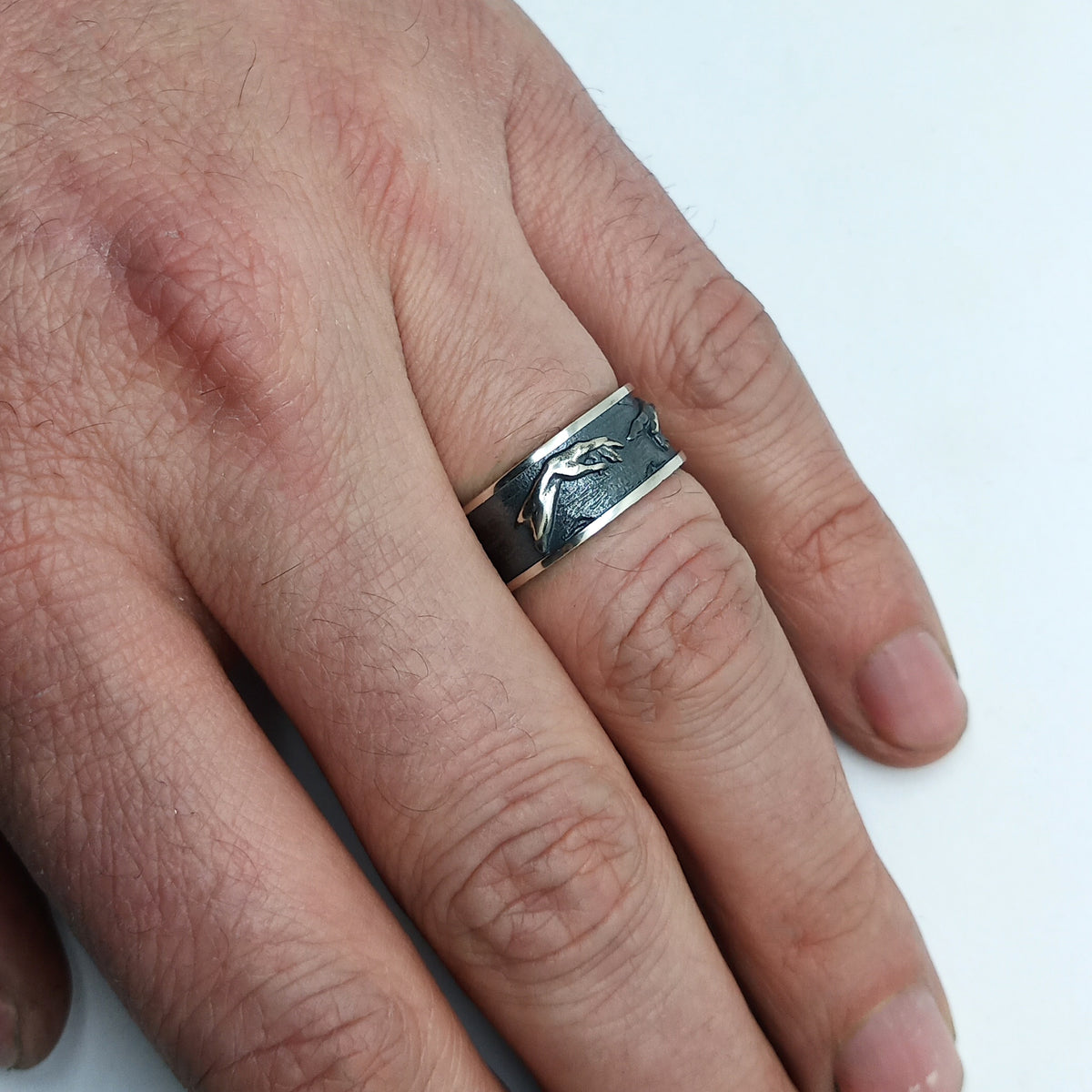 Hand-worn view showing the scale and blackened Creation of Adam relief on the men’s silver band — INDIGO Jewelry.