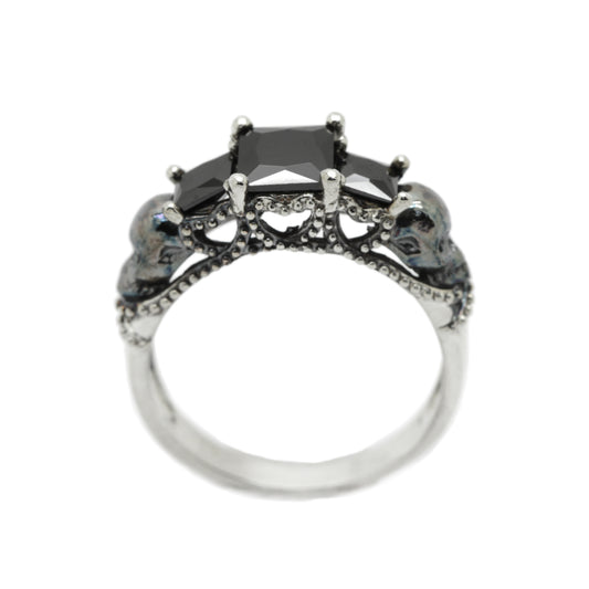 Gothic engagement ring for women featuring three square-cut black synthetic zircons and skull accents on both sides. Handcrafted in oxidized sterling silver with dark romantic style, ideal as a gothic promise ring, skull engagement ring, or goth wedding ring. Inspired by memento mori and Santa Muerte symbolism. Unique gothic jewelry for alternative brides who seek bold and symbolic design by INDIGO JEWELRY