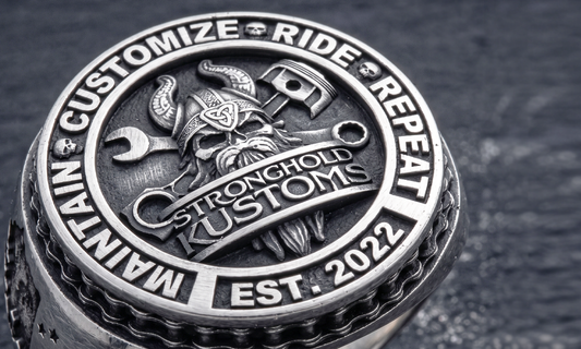 Close-up of a custom handcrafted silver biker signet ring with the Stronghold Kustoms logo, featuring intricate mechanical and viking-style engraving.