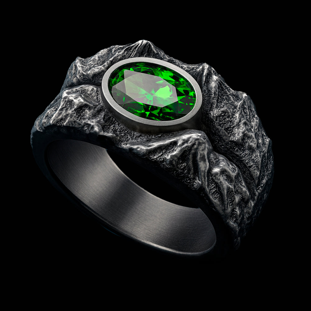 A silver ring with a large oval-shaped green gemstone set in the center, surrounded by a textured, rocky design.
