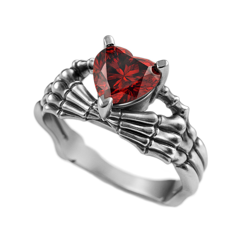 A silver ring with a red gemstone in the center, resembling a skeleton hand.
