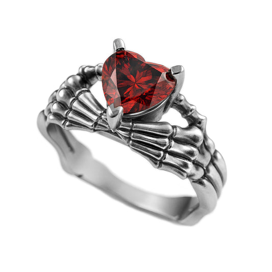 A silver ring with a red gemstone in the center, resembling a skeleton hand.