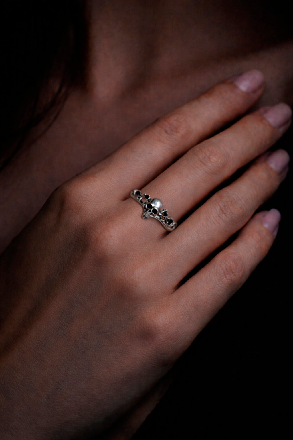 A close-up of a person's hand wearing a silver ring with a skull design.