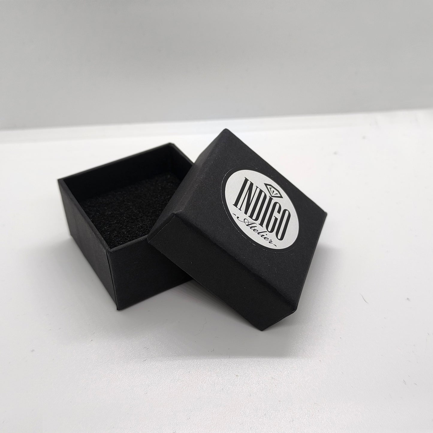 An open black jewelry box with a white circular logo on it, placed on a white surface.