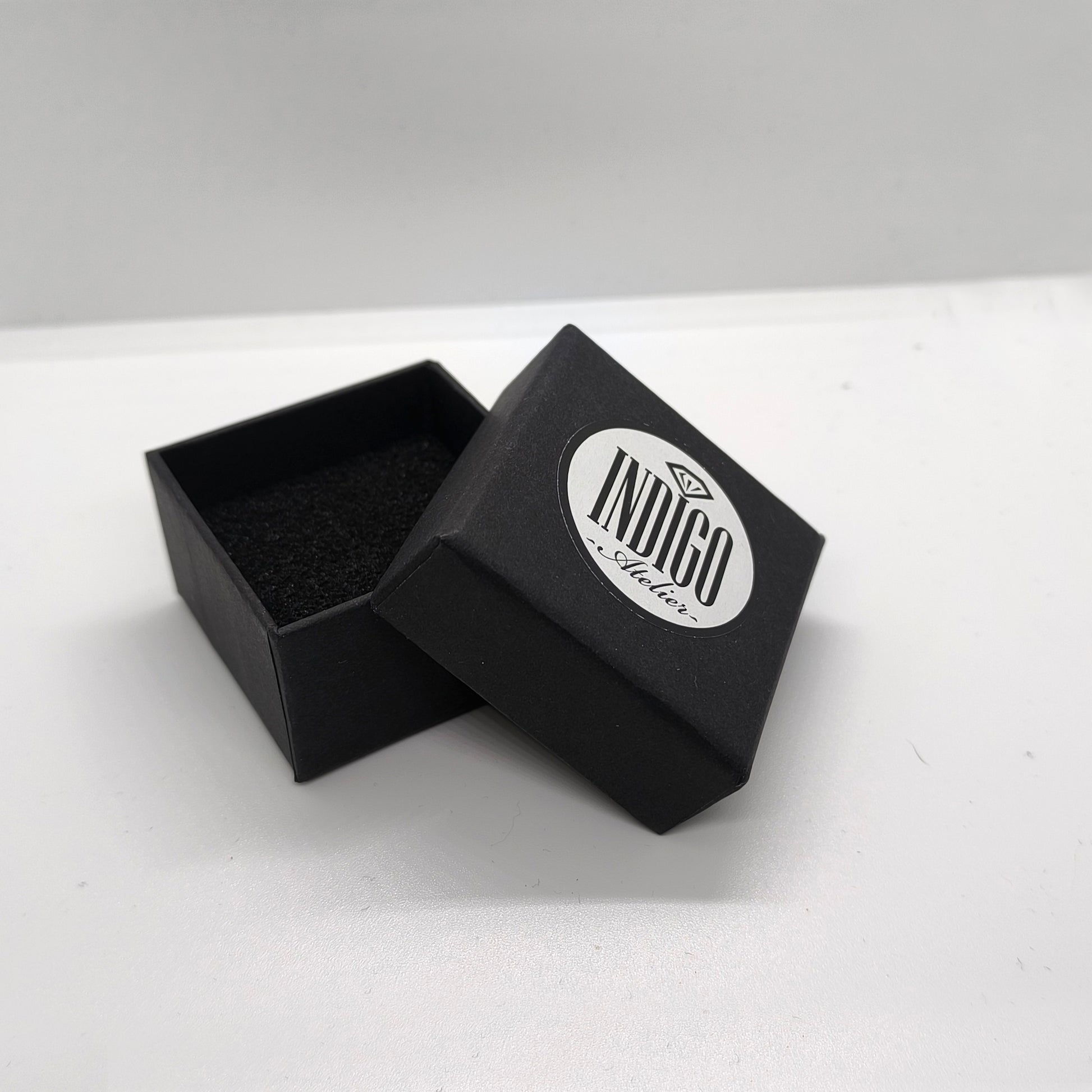 An open black jewelry box with a white circular logo on it, placed on a white surface.