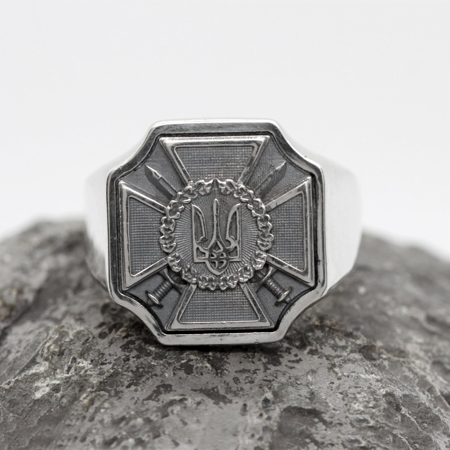 A silver ring with a decorative emblem featuring a crown and crossed swords.