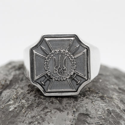 A silver ring with a decorative emblem featuring a crown and crossed swords.