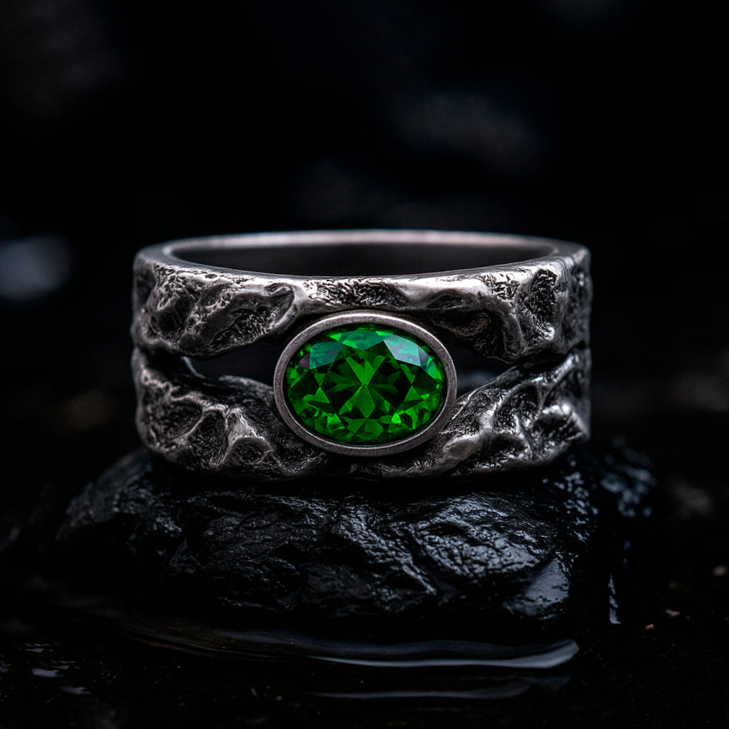 A silver ring with a large green gemstone, possibly a diamond, set in a textured metal band, placed on a black surface.
