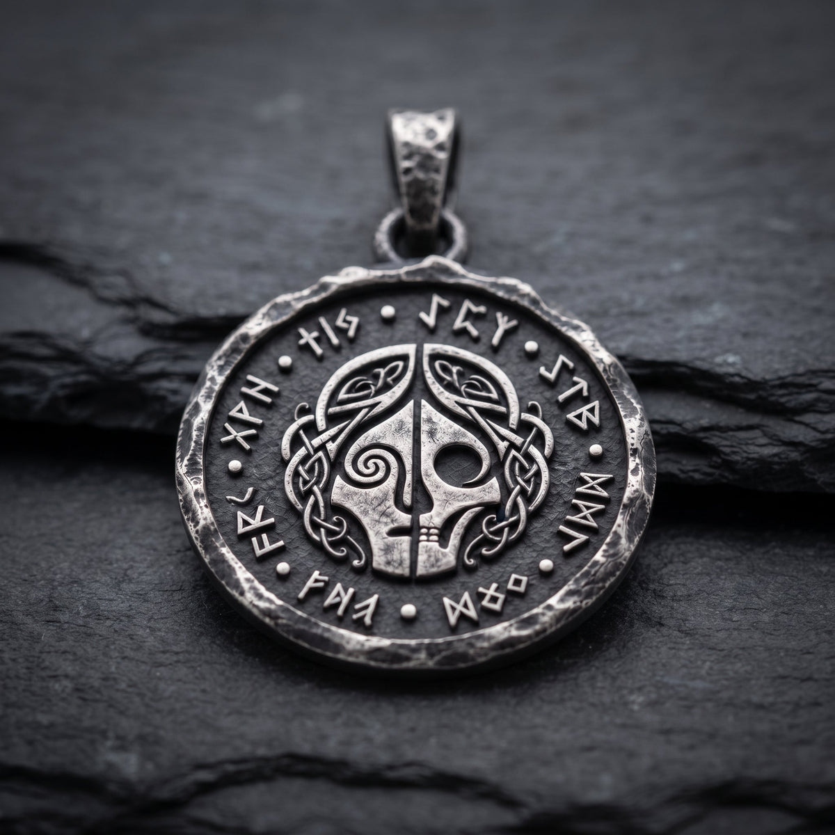Silver Hel pendant on dark slate, showing the divided face, runic circle and textured edge. INDIGO Jewelry.