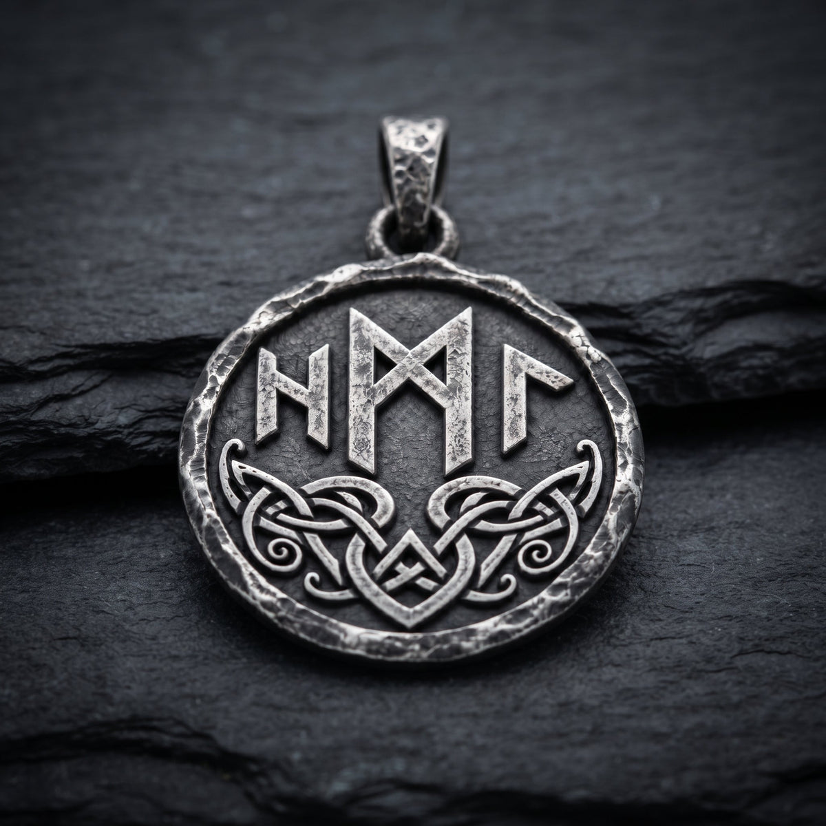 Reverse of the Hel pendant on dark slate, showing raised runes and interwoven ornament. INDIGO Jewelry.