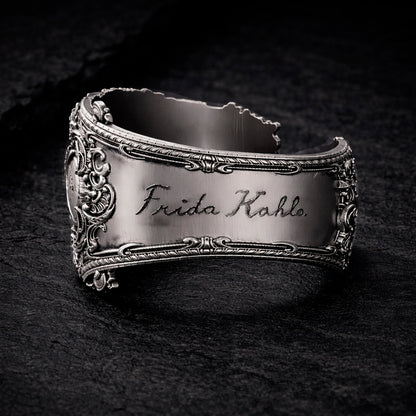 Open oxidized silver thumb ring featuring a detailed portrait of Frida Kahlo. Artistic spoon ring inspired by vintage silverware jewelry, designed as an open ring that wraps tightly around the thumb. Statement thumb ring with sculptural relief and darkened recessed details, handcrafted art jewelry. Frida Kahlo open ring made of blackened silver, bold spoon ring for the thumb, unique wearable art.