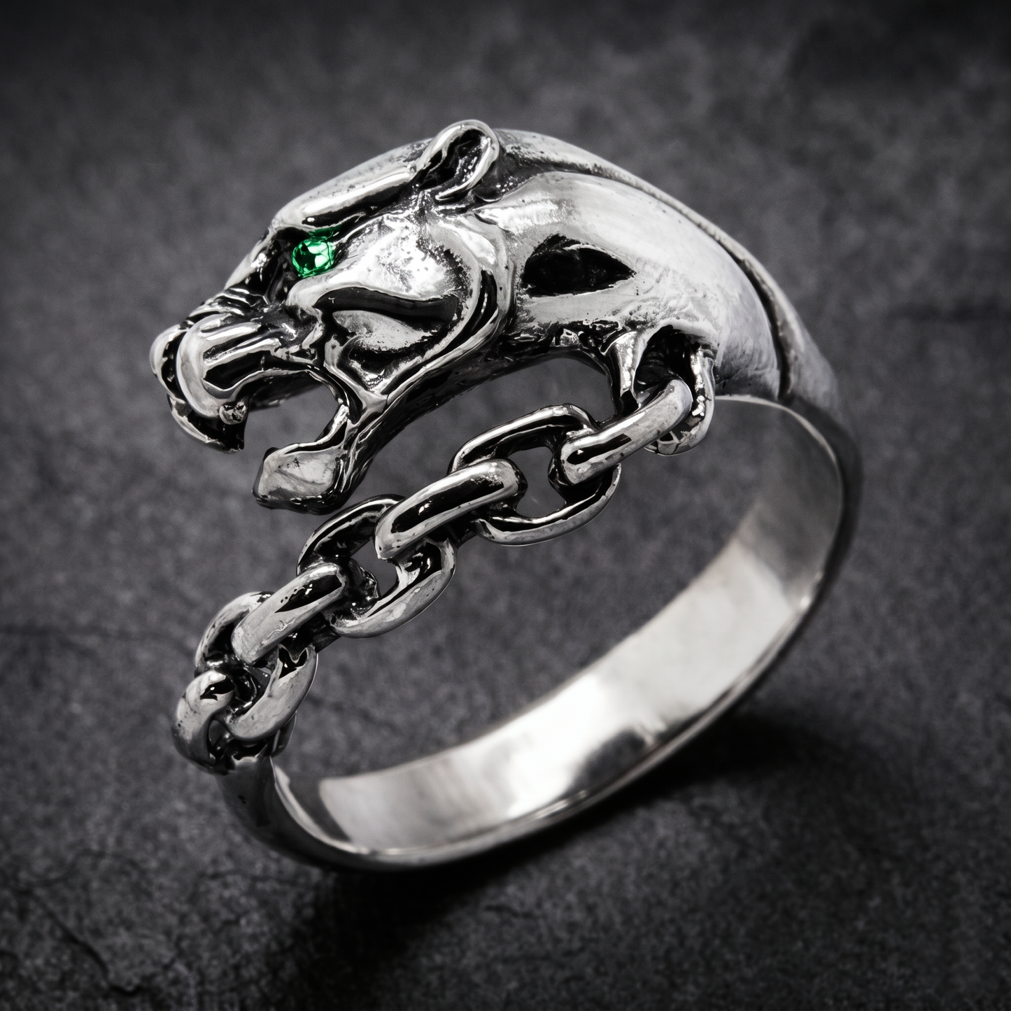 A silver ring with a silver Panthera head design and a chain-link chain attached to it. Green zircon in the eye. Indigo Jewelry.
