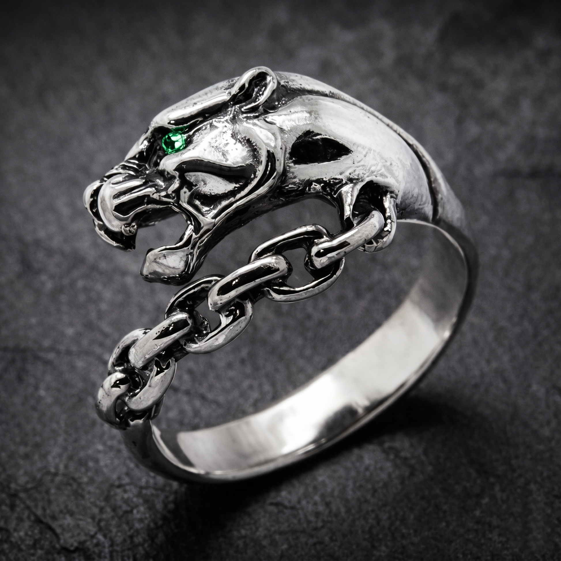 A silver ring with a silver Panthera head design and a chain-link chain attached to it. Green zircon in the eye. Indigo Jewelry.