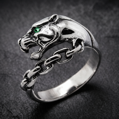 A silver ring with a silver Panthera head design and a chain-link chain attached to it. Green zircon in the eye. Indigo Jewelry.