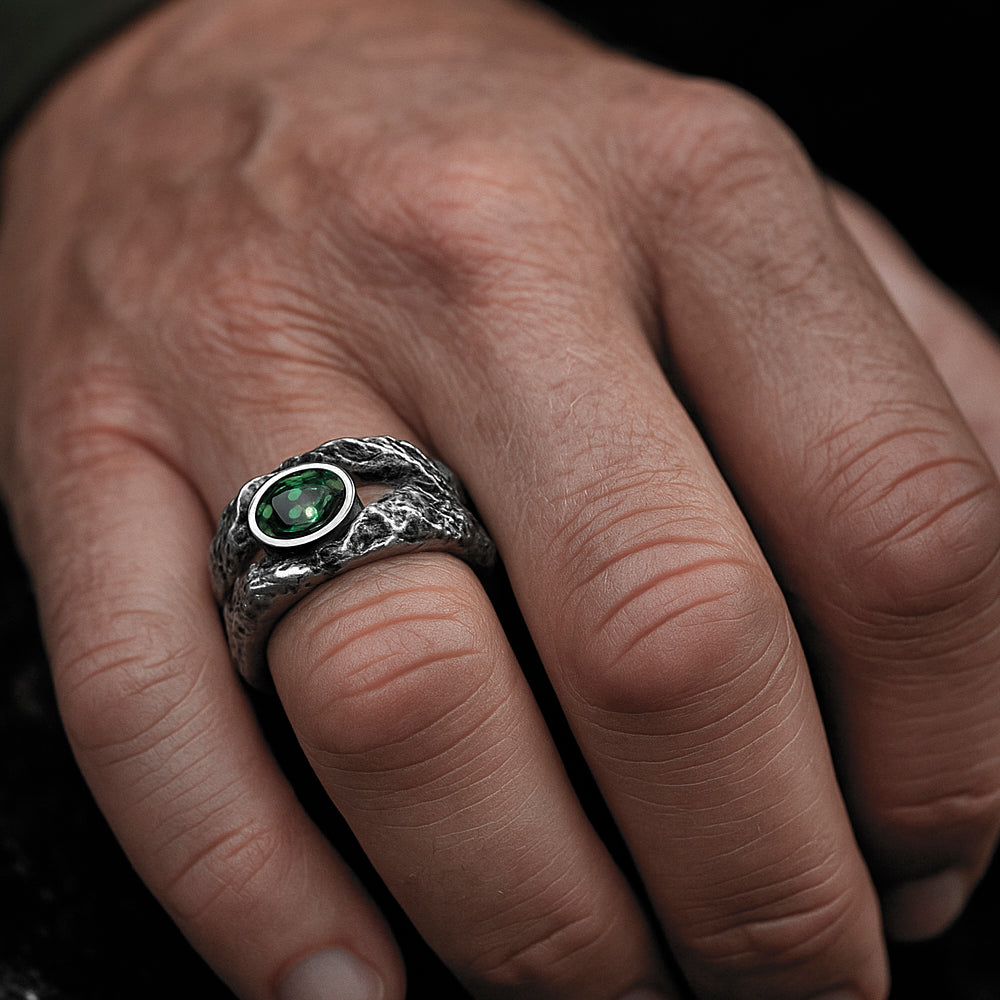 A close-up of a person's hand wearing a silver ring with a green gemstone.