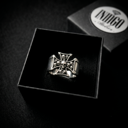 A silver ring with a skull and crossbones design is displayed in a black box, with a logo visible in the background.