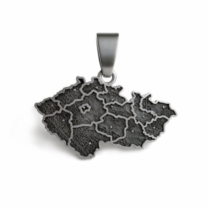 A handcrafted sterling silver pendant shaped like the map of the Czech Republic with the engraved phrase “Já❤️Česko.” The pendant measures 27 mm in width and 24 mm in height with the bail, weighs 3 g, and features a smooth polished edge with dark engraved details. It is displayed resting on a soft dark fabric cushion with gentle lighting that highlights the texture of the metal and the elegant contours of the design.
