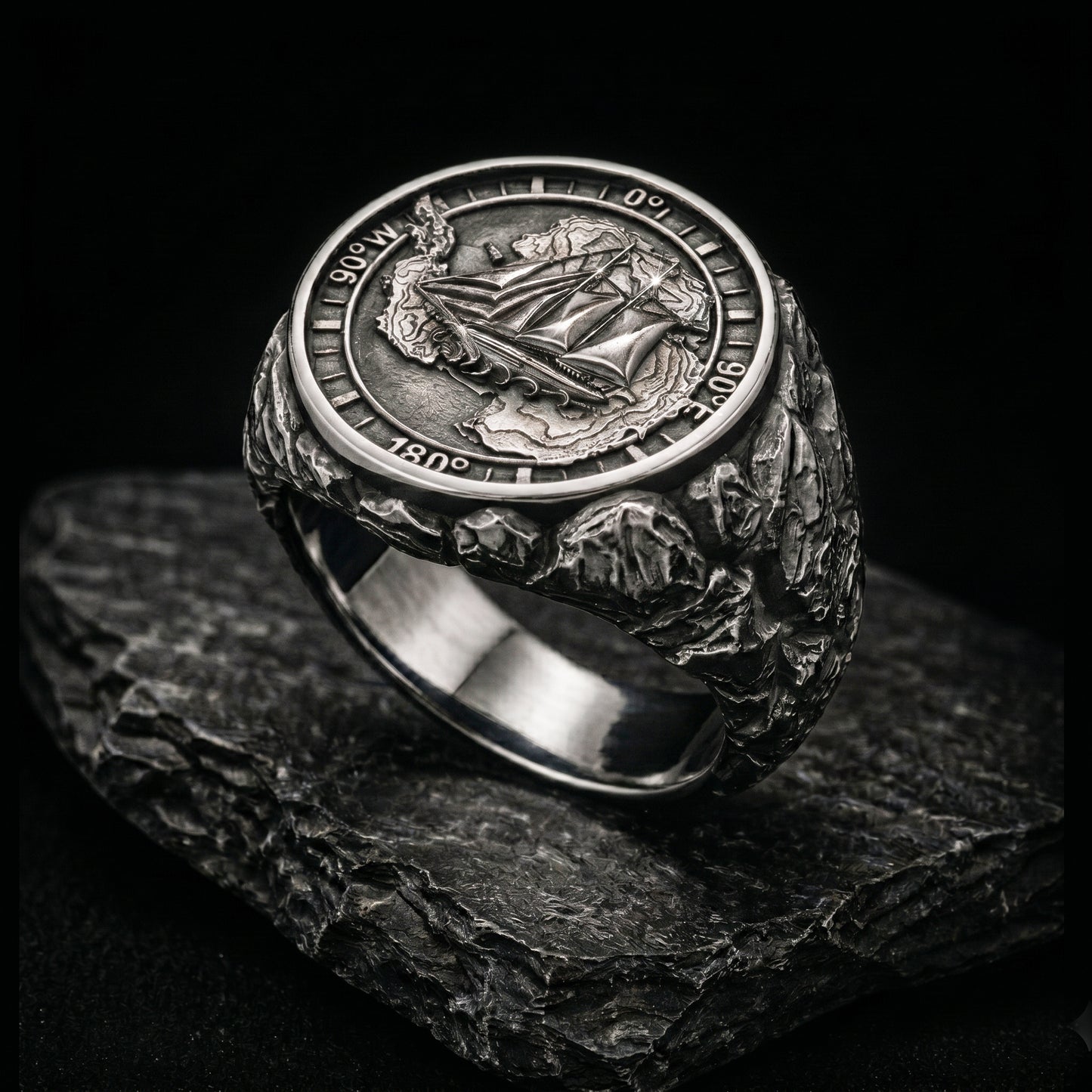 Antarctica explorer signet ring in solid sterling silver 925 featuring a detailed sailing ship over a map of Antarctica, surrounded by directional markings. The ring has a deep oxidized finish with strong contrast, highlighting fine handcrafted textures and relief details. Shot on a dark stone background to emphasize its bold, masculine design, adventure theme, and expedition spirit. Unique nautical jewelry piece inspired by travel, ocean journeys, and exploration beyond the known world.