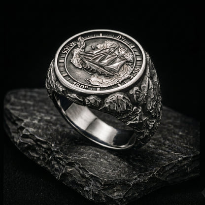 Antarctica explorer signet ring in solid sterling silver 925 featuring a detailed sailing ship over a map of Antarctica, surrounded by directional markings. The ring has a deep oxidized finish with strong contrast, highlighting fine handcrafted textures and relief details. Shot on a dark stone background to emphasize its bold, masculine design, adventure theme, and expedition spirit. Unique nautical jewelry piece inspired by travel, ocean journeys, and exploration beyond the known world.