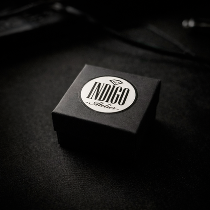 A black and white image of a small, square-shaped box with a white circular label on it, placed on a dark surface.