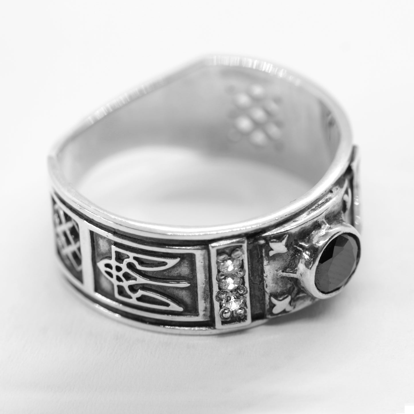 A silver ring with intricate designs and a large black gemstone.
