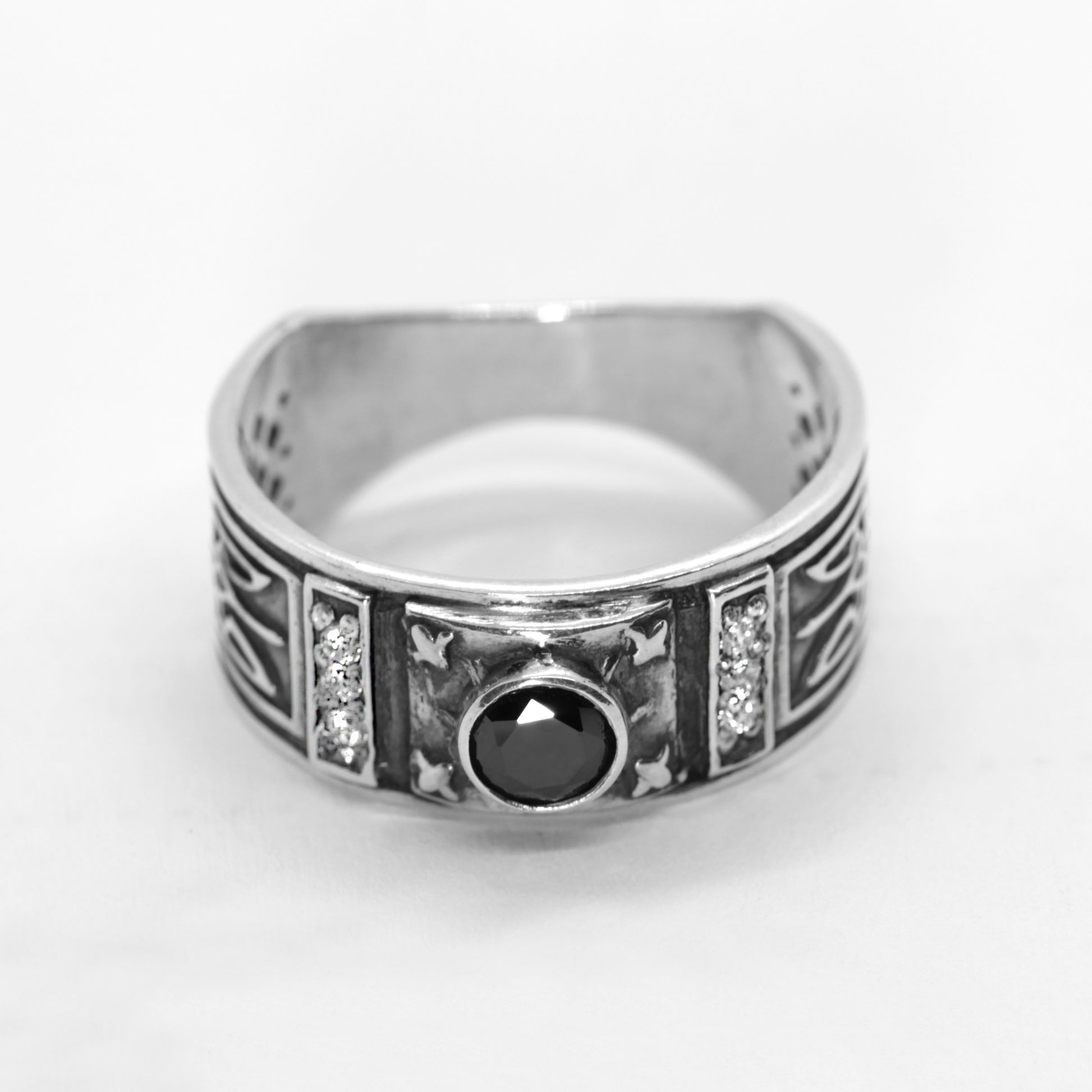 A silver ring with a black gemstone in the center, surrounded by decorative elements.