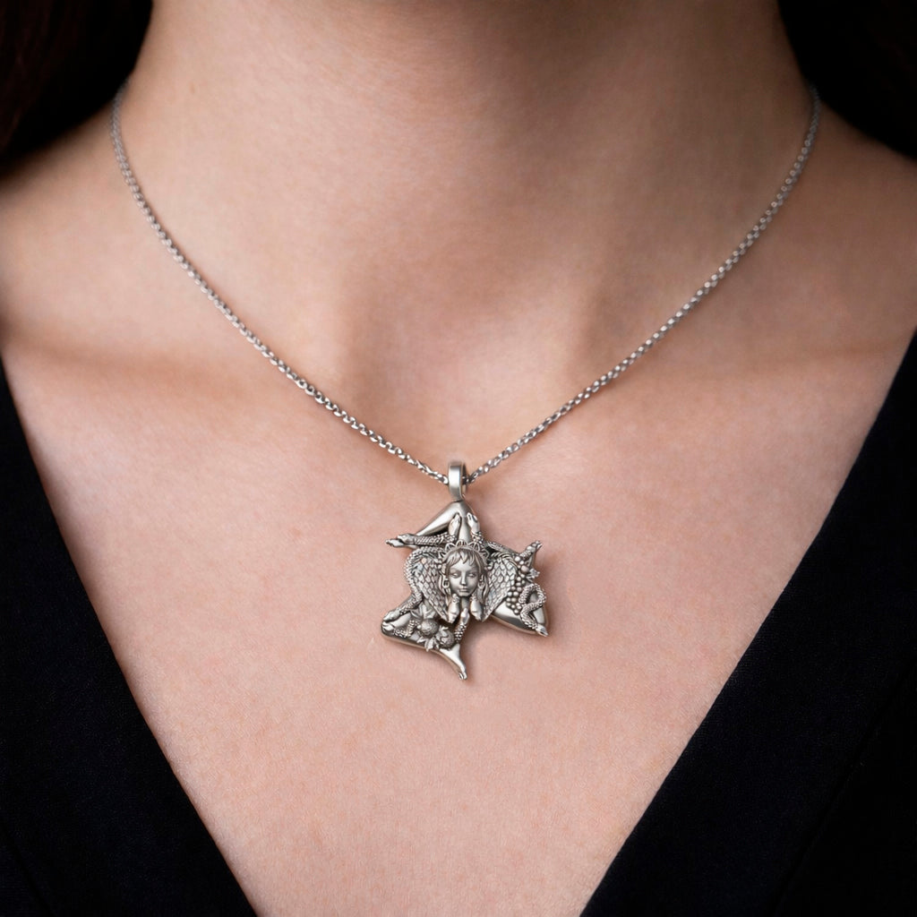 Detailed view of a handcrafted sterling silver Trinacria pendant by Indigo Jewelry. The design features a central Medusa Gorgon head with expressive facial features, surrounded by three bent running legs and interwoven stalks of wheat, symbolizing Sicilian heritage and fertility. The oxidized silver finish highlights the intricate mythological textures. This authentic Mediterranean protection amulet is shown as a high-quality statement piece for women's jewelry collections.