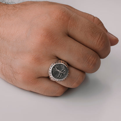 A close-up image of a hand wearing a silver ring with a tree design.