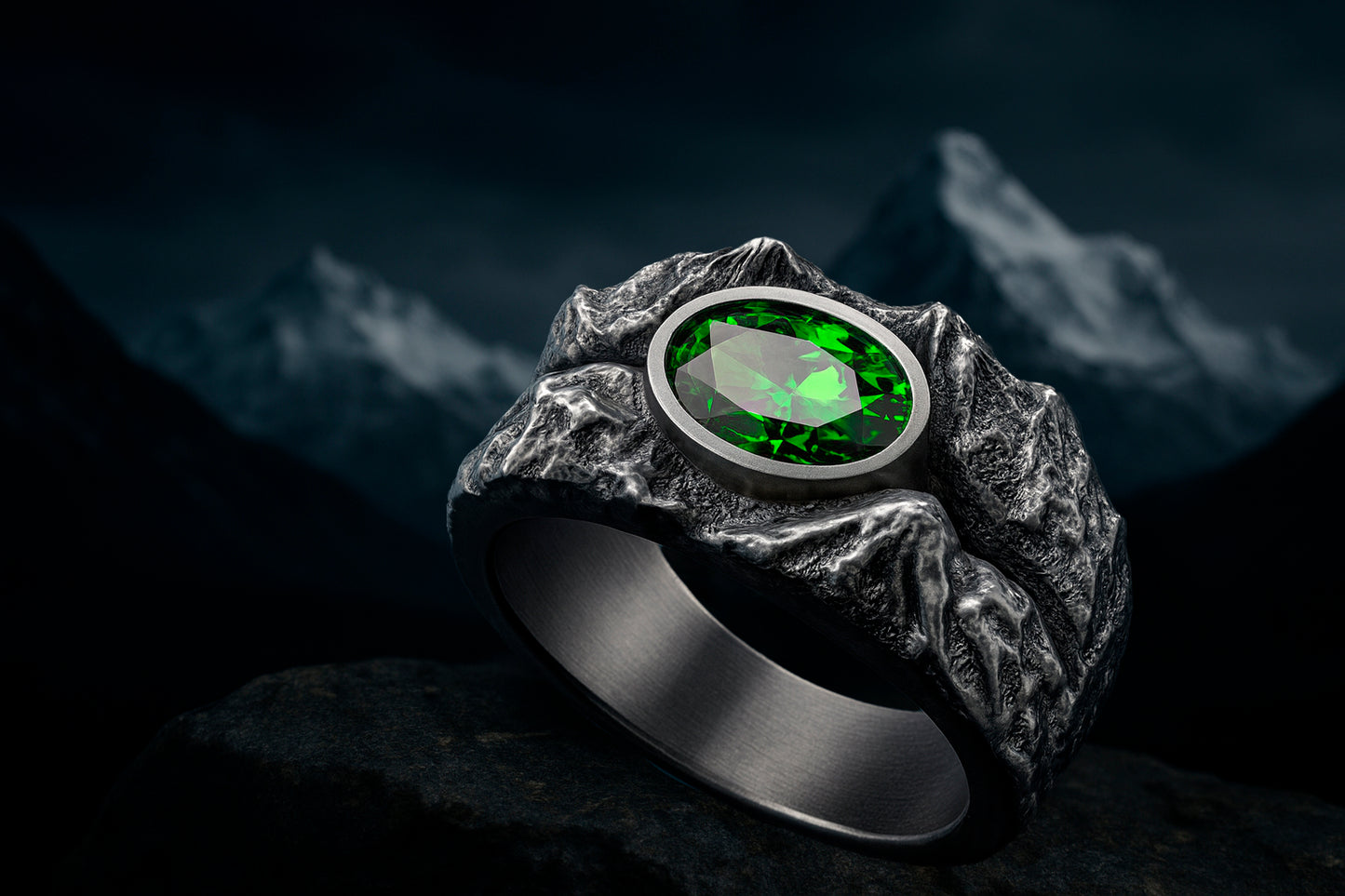 A silver ring with a large oval-shaped green gemstone is displayed against a dark, mountainous background.
