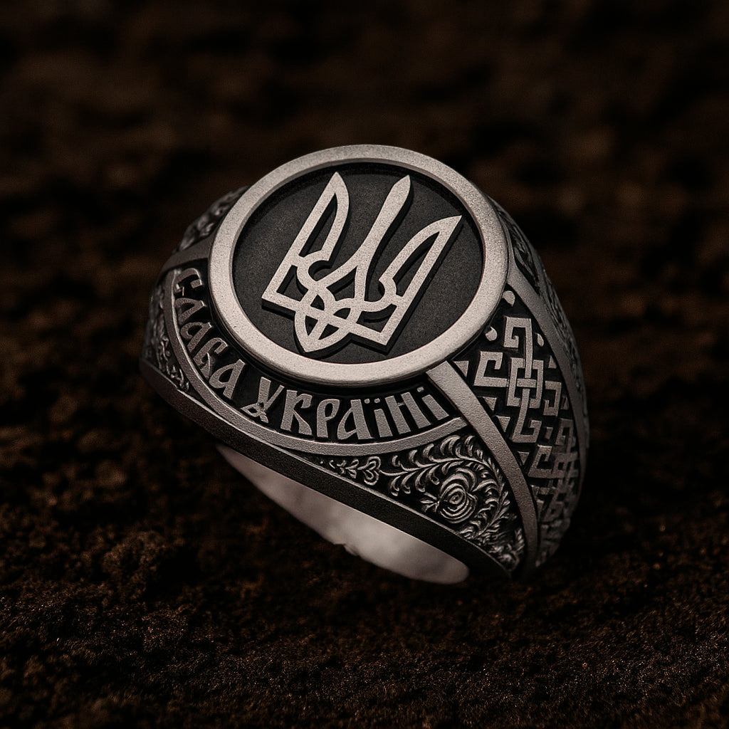 A silver ring with intricate designs and a central emblem, resting on a dark surface.