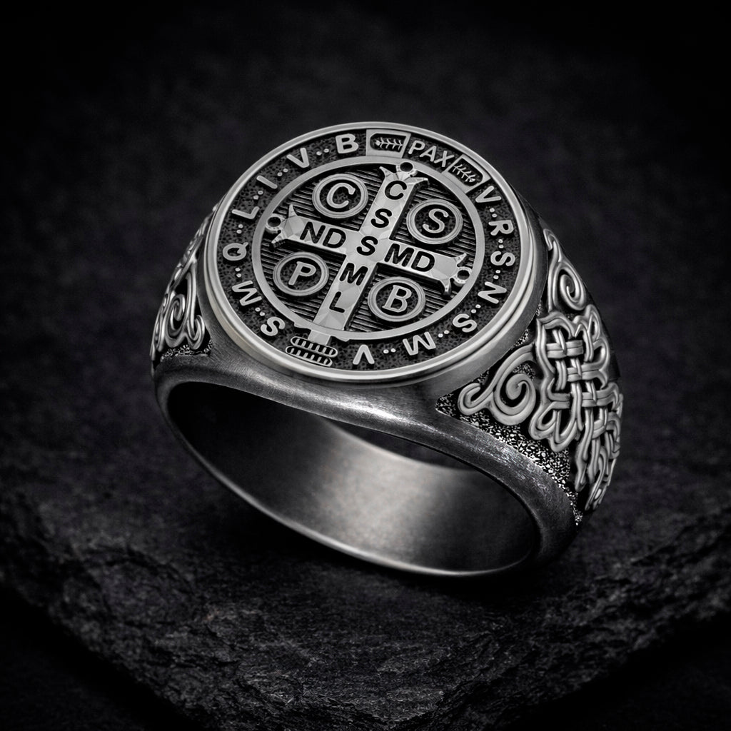 A silver ring with a circular design featuring the letters C, S, V, B, and P in a cross shape, surrounded by various other symbols and text.