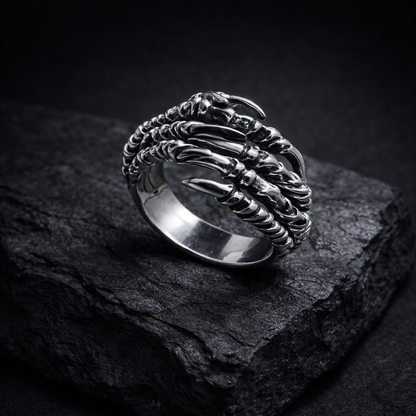 A silver ring with claws and claws design sits on a dark surface, creating a striking contrast.