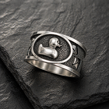 A silver ring with a metal duck design on a textured surface.