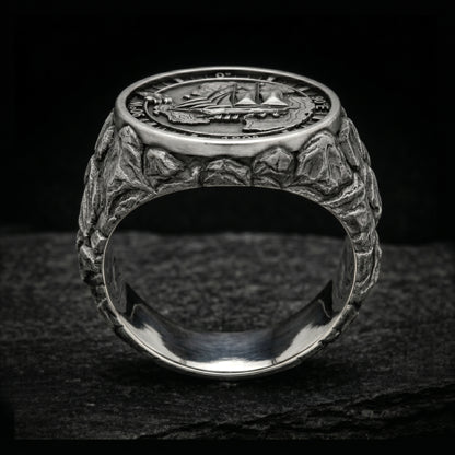 Antarctica explorer signet ring in solid sterling silver 925 featuring a detailed sailing ship over a map of Antarctica, surrounded by directional markings. The ring has a deep oxidized finish with strong contrast, highlighting fine handcrafted textures and relief details. Shot on a dark stone background to emphasize its bold, masculine design, adventure theme, and expedition spirit. Unique nautical jewelry piece inspired by travel, ocean journeys, and exploration beyond the known world.