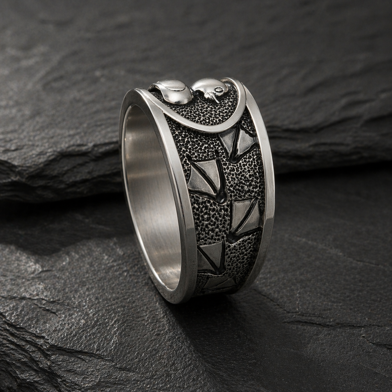 A silver ring with a unique, intricate design sits on a dark surface.