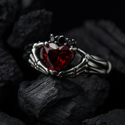 A ring with a red gemstone, resembling a heart, is displayed against a dark background, with a skeletal hand holding the gemstone.