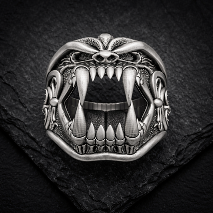A close-up black and white image of a silver ring with a fierce, menacing design featuring sharp teeth and claws.