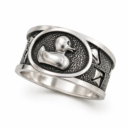 Sterling silver duck signet ring with oxidized textured background and polished raised duck symbol. Wide band design with detailed engraving and strong contrast. Minimalist yet expressive jewelry piece photographed on clean background and lifestyle scenes, including close-up macro views and on-hand shots. Designed as a unique statement ring for men and women, combining craftsmanship, symbolism, and modern style.