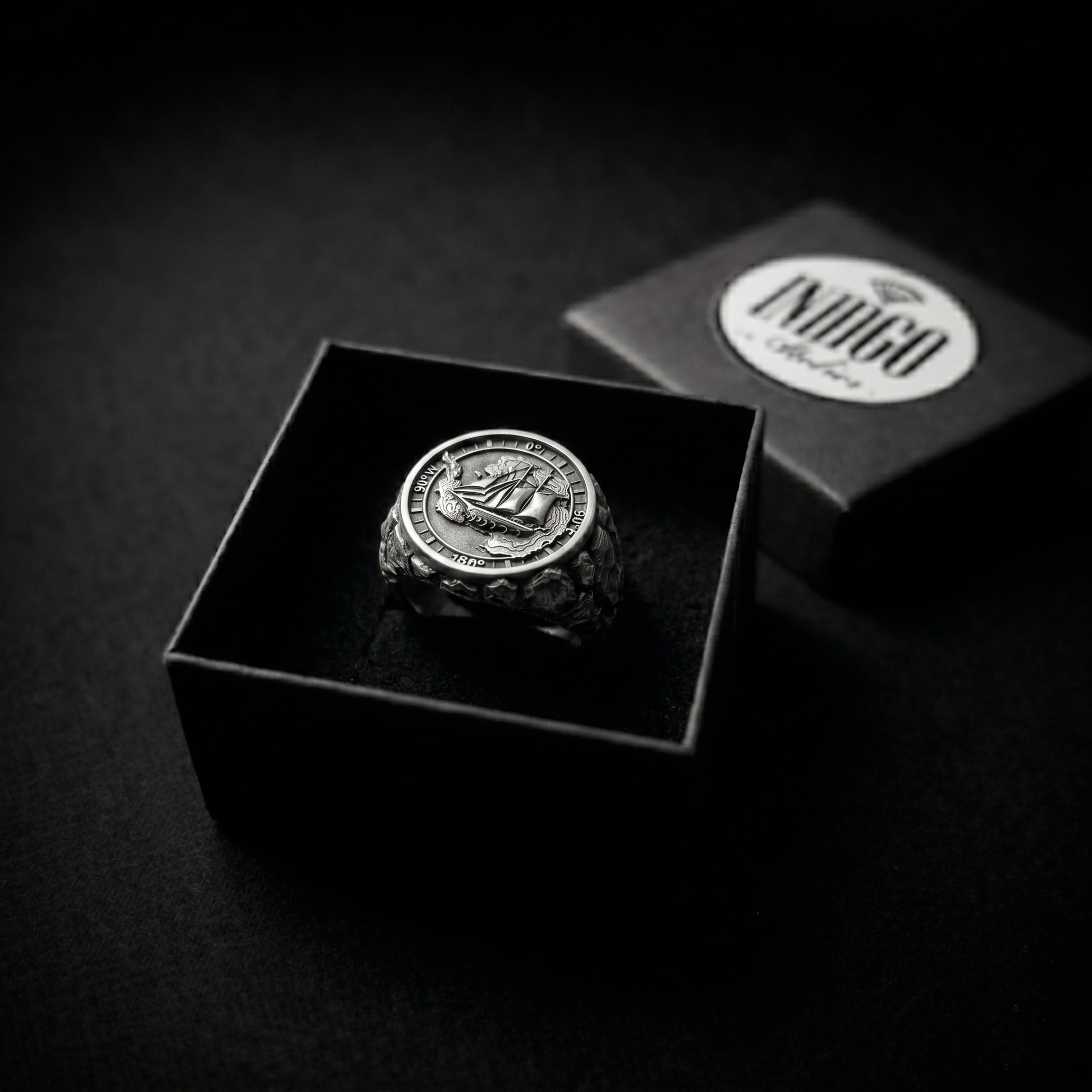 Antarctica explorer signet ring in solid sterling silver 925 featuring a detailed sailing ship over a map of Antarctica, surrounded by directional markings. The ring has a deep oxidized finish with strong contrast, highlighting fine handcrafted textures and relief details. Shot on a dark stone background to emphasize its bold, masculine design, adventure theme, and expedition spirit. Unique nautical jewelry piece inspired by travel, ocean journeys, and exploration beyond the known world.