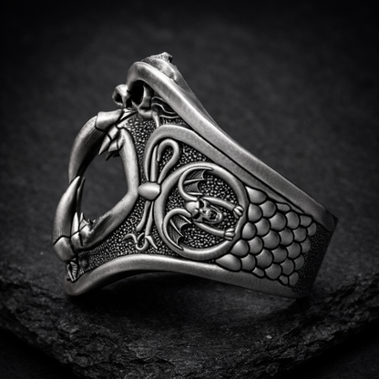 A detailed silver ring with an intricate design featuring a bat-like creature and a skull-like figure.