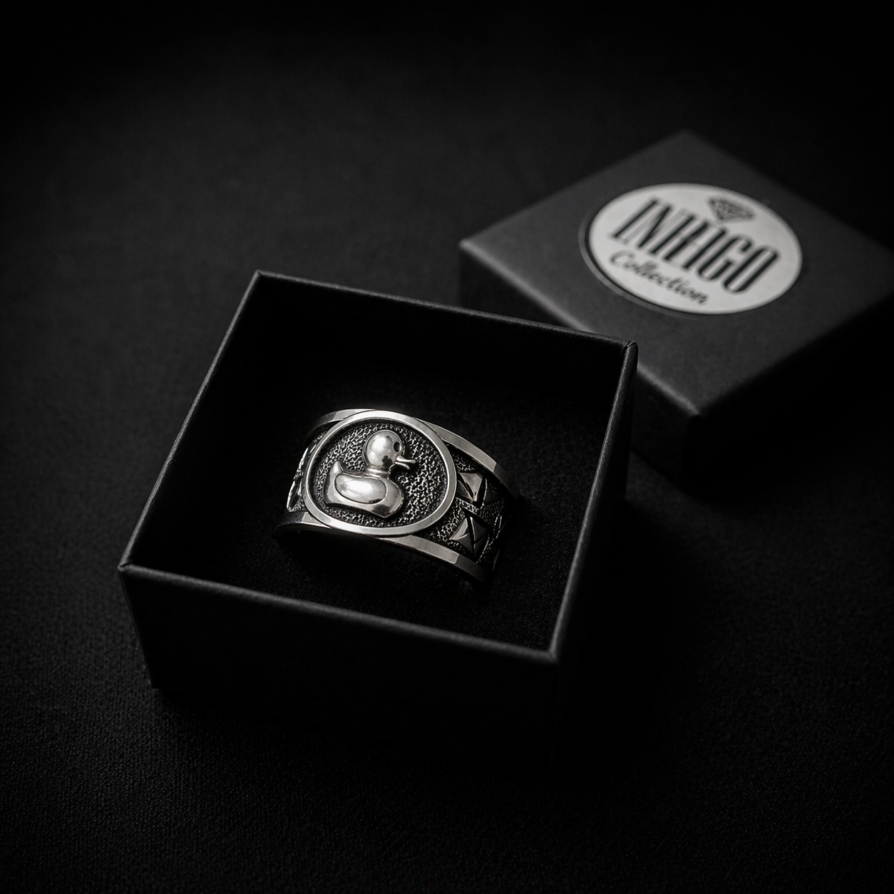 A silver ring with a duck design is displayed in a black jewelry box, with the box's lid visible in the background.