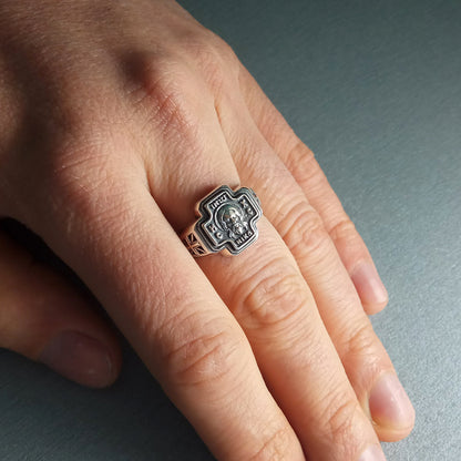 A close-up of a person's hand wearing a silver ring with a skull design.