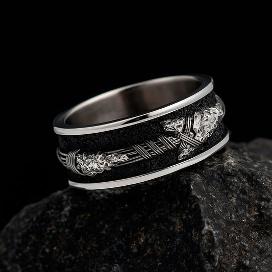 A silver ring with a black and white design sits on a dark rock.