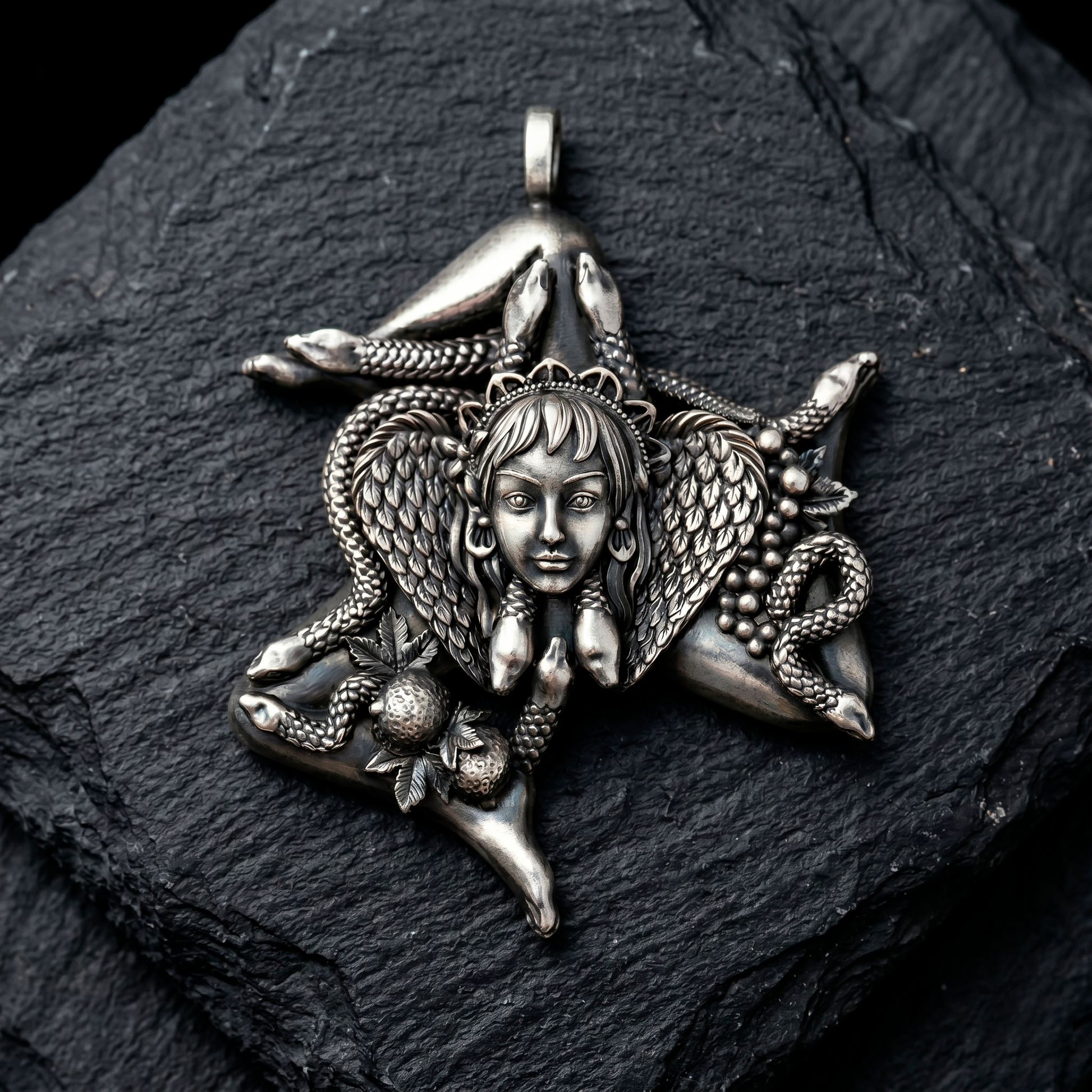 A silver-colored pendant featuring a detailed design of a woman's face surrounded by snakes and other fantastical elements. Trinacria Sicily Pendant Sterling Silver Necklace on Dark Stone Background - INDIGO Jewelry