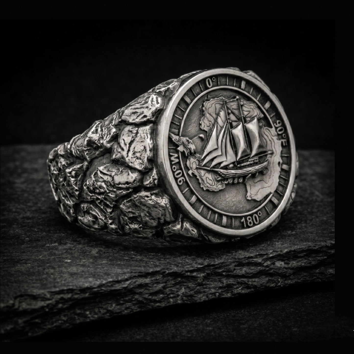 Antarctica explorer signet ring in solid sterling silver 925 featuring a detailed sailing ship over a map of Antarctica, surrounded by directional markings. The ring has a deep oxidized finish with strong contrast, highlighting fine handcrafted textures and relief details. Shot on a dark stone background to emphasize its bold, masculine design, adventure theme, and expedition spirit. Unique nautical jewelry piece inspired by travel, ocean journeys, and exploration beyond the known world.