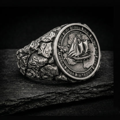 Antarctica explorer signet ring in solid sterling silver 925 featuring a detailed sailing ship over a map of Antarctica, surrounded by directional markings. The ring has a deep oxidized finish with strong contrast, highlighting fine handcrafted textures and relief details. Shot on a dark stone background to emphasize its bold, masculine design, adventure theme, and expedition spirit. Unique nautical jewelry piece inspired by travel, ocean journeys, and exploration beyond the known world.