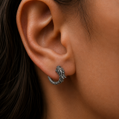 Close-up lifestyle photograph of a handcrafted dragon hoop earring in oxidized sterling silver 925 by INDIGO Jewelry, worn on the ear. Features a detailed dragon head, textured scales, and a lightly blackened silver finish for a vintage gothic look. Small fantasy-inspired silver hoop earring with medieval and mythical aesthetics, designed as a bold yet elegant statement piece for gothic, alternative, and symbolic jewelry lovers.